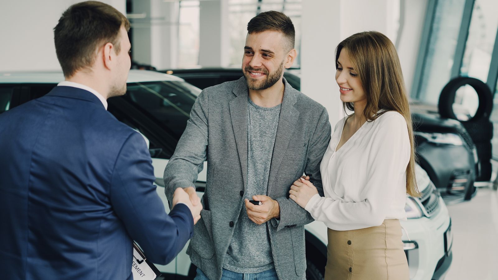 Paar besiegelt den Autokauf mit dem Verkaeufer im Showroom eines Autohauses